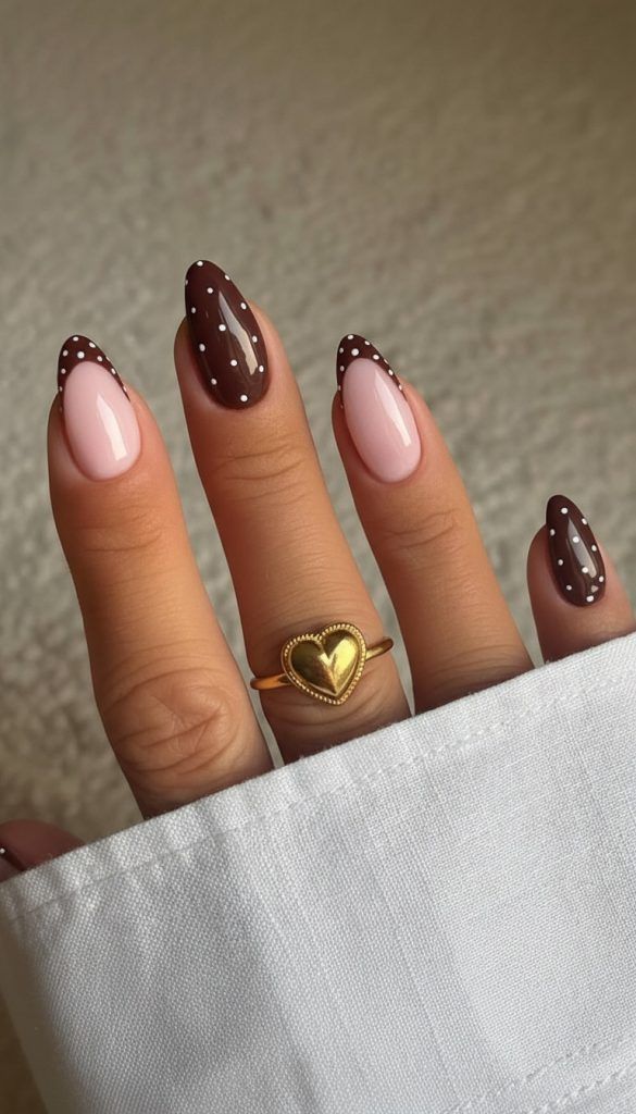 Close-up of a hand with almond-shaped nails featuring a polka-dot French manicure and a solid polka-dot nail, wearing a…