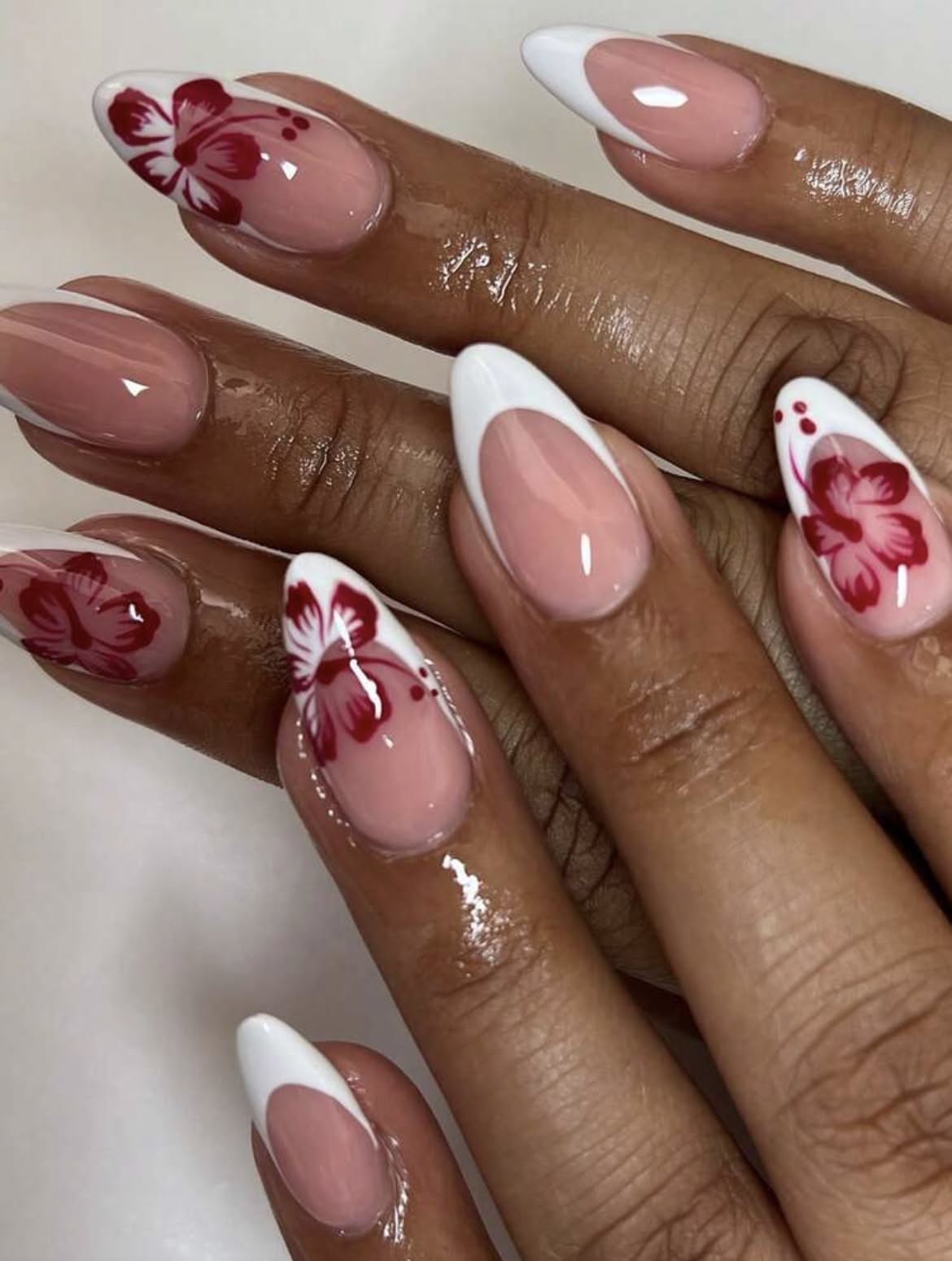 Close-up of manicured hands with almond-shaped nails featuring white French tips and red floral designs on some nails.