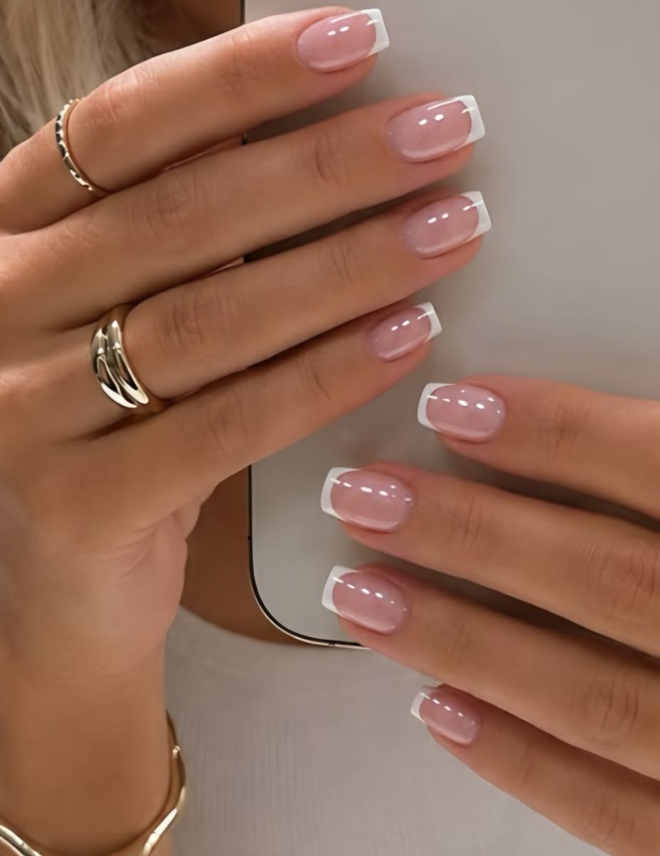 Close-up of a person's hands holding a phone, showcasing short nails with a classic French manicure.