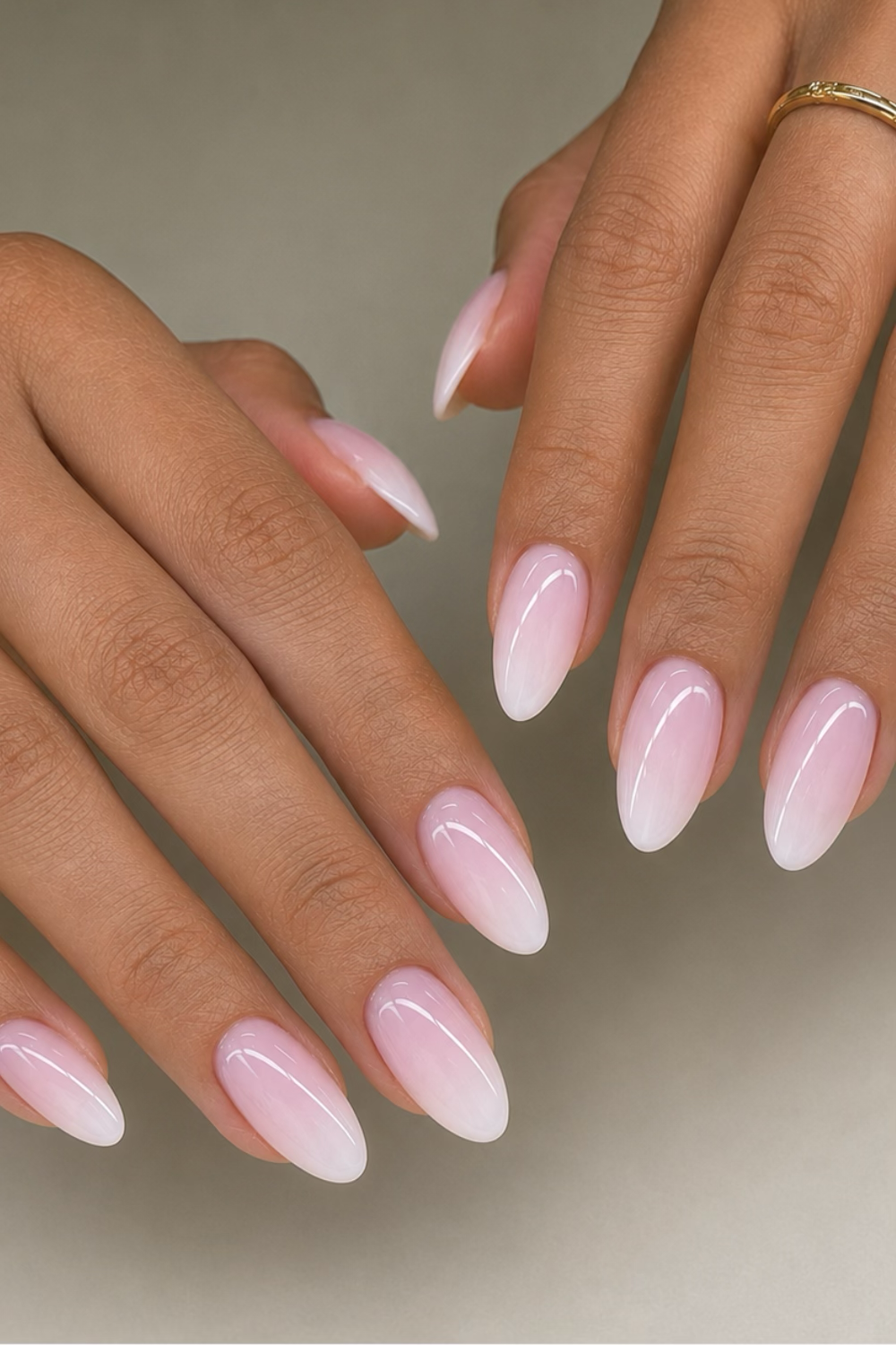 Close-up of a person's hands with almond-shaped nails featuring a delicate pink ombre design fading to white at the tips.