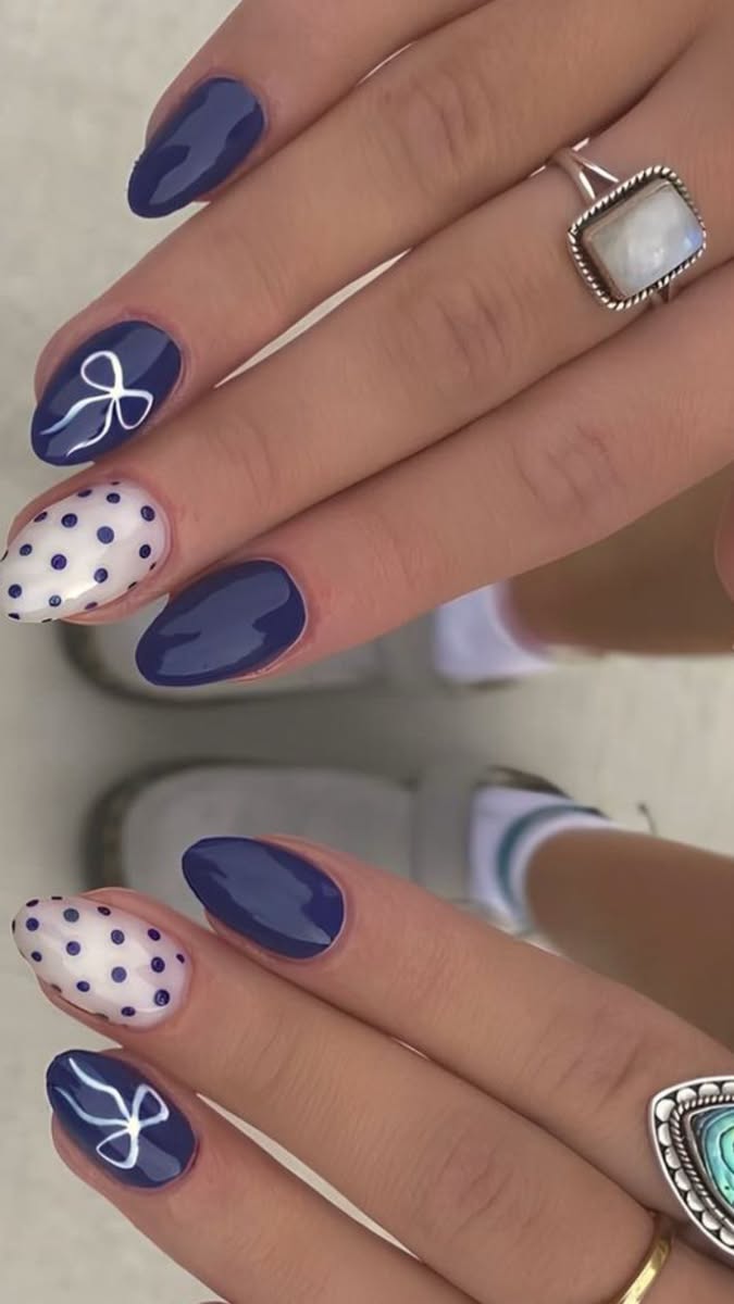 Hands with short navy blue nails, some featuring white polka dots and others a white bow design.