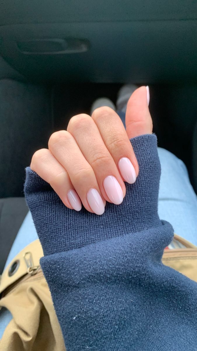 A hand with oval-shaped, light pink manicured nails, wearing a dark blue sleeve, seen in a car.