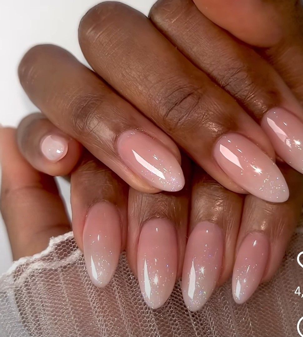 Close-up of manicured hands with pink nails featuring a subtle glitter fade from the tips.