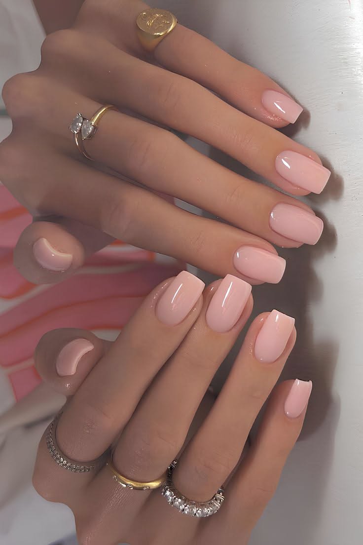 Close-up of manicured hands with short, square-tipped nails painted in a soft, glossy blush pink.