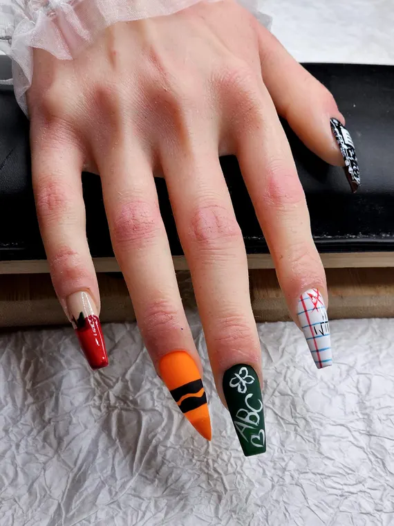 Long colorful school-themed press-on nails with pencil, crayon, notebook, and alphabet designs.