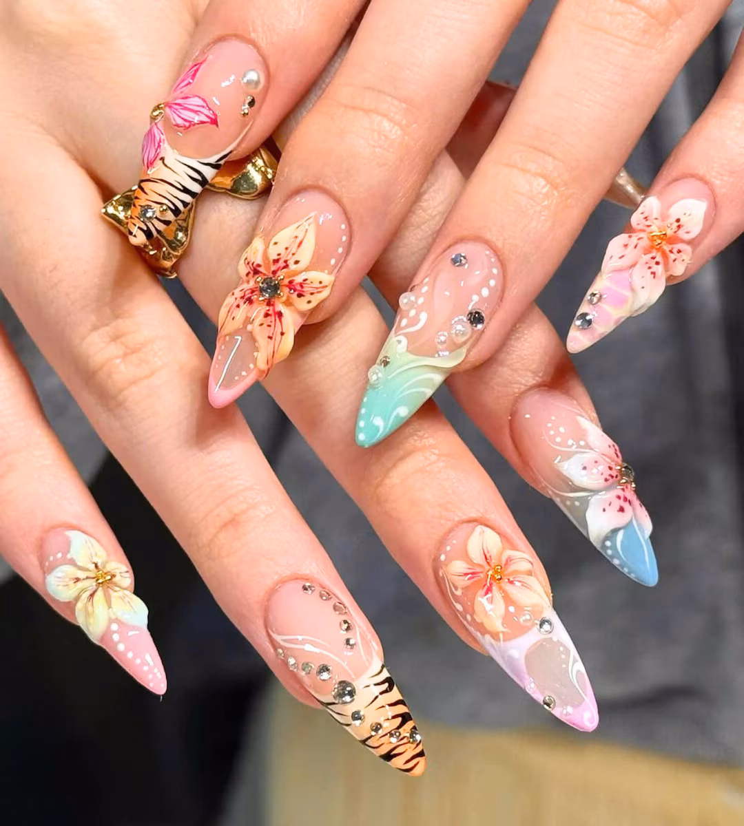 Long stiletto press-on nails with colorful floral decorations, rhinestones, and animal-print accents.